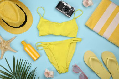 Açık mavi arka planda mayolu ve plaj aksesuarlı düz bir kompozisyon.