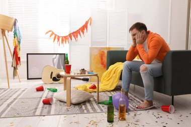 Parti sonrası dağınık odada kanepede yorgun sarhoş bir adam.