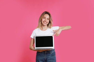 Pembe arka planda modern dizüstü bilgisayarı olan genç bir kadın.