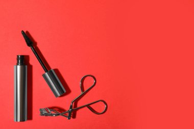 Kırmızı arka planda siyah rimel ve kirpik bigudisi, metin için yeri olan düz bir yer. Makyaj ürünü