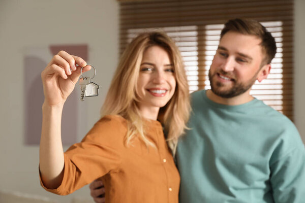 Happy young couple with key in new house, focus on hand