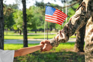 Asker ve Amerikan bayrağıyla dışarıda el ele tutuşan küçük oğlu, yakın plan. ABD 'de Gaziler Günü