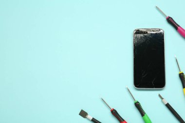 Açık mavi arka planda hasarlı akıllı telefon ve tamir aleti, düz konum. Metin için boşluk