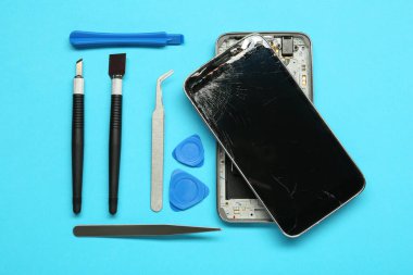 Açık mavi arkaplanda hasarlı akıllı telefon ve tamir aracı, düz yatar