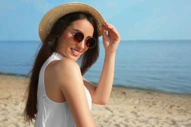 Plajda hasır şapkalı ve güneş gözlüklü güzel bir genç kadın. Şık başlık