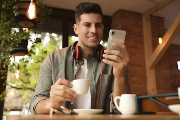 一个英俊的男人 早上在咖啡店里喝着咖啡和智能手机 — 图库照片