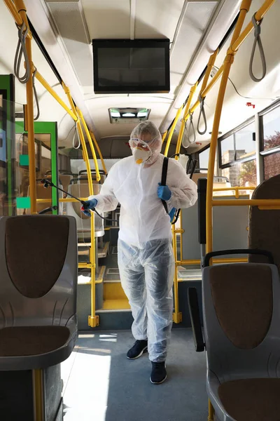 Public transport sanitation. Worker in protective suit disinfecting bus salon