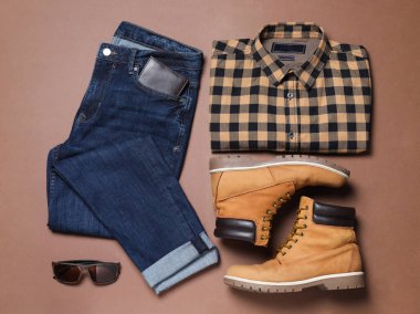 Kahverengi arka planda şık erkek kıyafetleri ve çizmeleri olan düz bir kompozisyon.