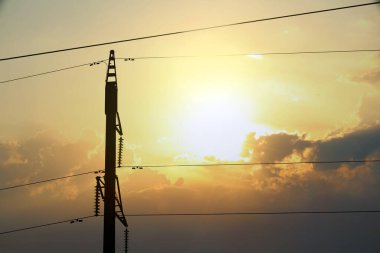 Güneşli bir günde telefon direğinin silueti ve kablolar.