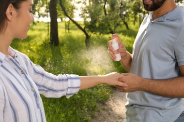 Parkta kız arkadaşının koluna böcek kovucu uygulayan bir adam, yakın plan. Kene ısırığı önleme