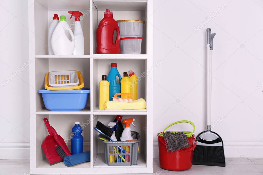 Shelving unit with detergents and cleaning tools near white wall indoors