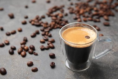 Bir fincan lezzetli espresso ve kahve çekirdekleri gri masada. Metin için boşluk