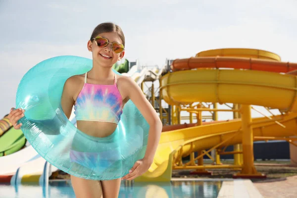 Cute little girl with inflatable ring near pool in water park, space for text
