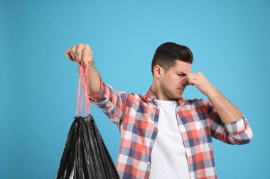 Açık mavi arka planda çöp torbası tutan adam.