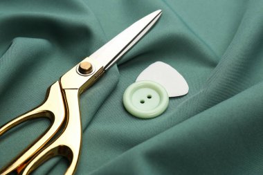 Yeşil kumaşta makas, düğme ve terzi tebeşiri, yakın plan.