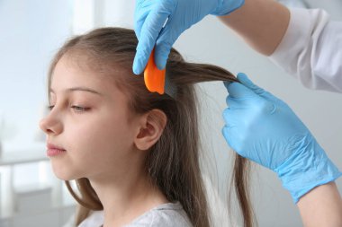 Klinikte kızın saçında bit tarağı kullanan bir doktor. Bit önleyici tedavi