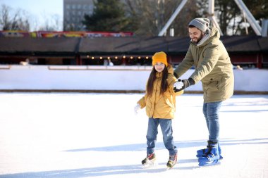 Baba ve kızı birlikte buz pateni pistinde vakit geçiriyorlar.