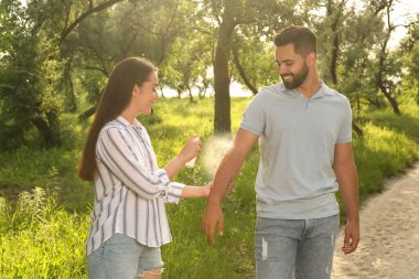 Woman applying insect repellent on her boyfriend's arm in park. Tick bites prevention