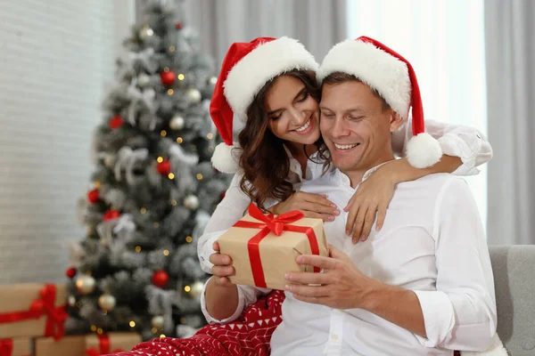 ハッピーカップルでサンタ帽子クリスマスギフトとともに自宅 — ストック写真