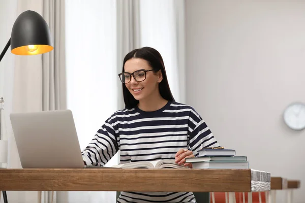 Young woman with laptop studying at table in library