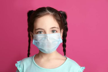 Pembe arka planda koruyucu maske takan bir kız. Çocuğun virüsten korunması