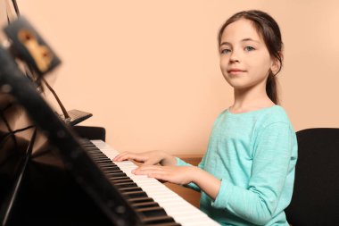 Bej duvarın yanında piyano çalan tatlı küçük bir kız. Müzik dersi