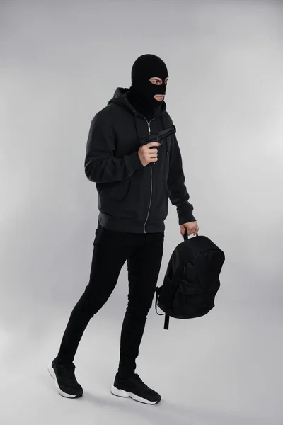 Mann Trägt Schwarze Sturmhaube Mit Rucksack Und Pistole Auf Hellgrauem — Stockfoto