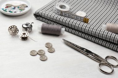 Beyaz ahşap masa üzerinde farklı dikiş malzemesi ve kumaş bileşimi.