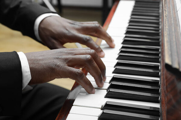 African-American man playing piano indoors, closeup. Talented musician