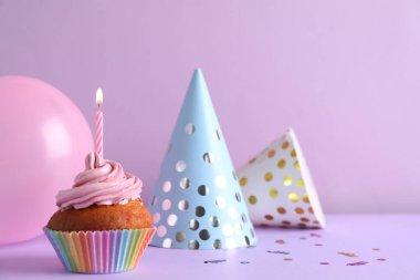 Parti şapkalarının yanında mum ve menekşe arka planında balon olan enfes bir doğum günü keki. Mesaj için yer var.