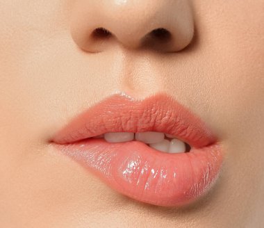 Gri arka planda dudaklarını ısıran güzel bir genç kadın. Yakın plan.