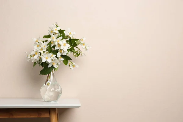 Bukiet Pięknych Kwiatów Jaśminu Szklanym Wazonie Stole Przy Beżowej Ścianie — Zdjęcie stockowe