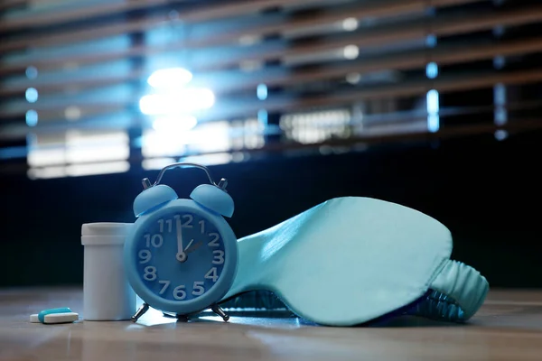 Alarm clock, sleeping mask and pills on table indoors. Insomnia treatment