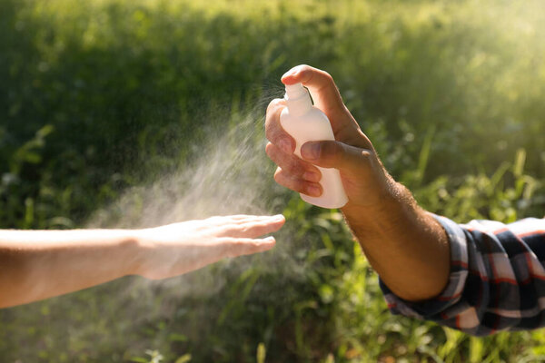 Отец распыления клещей репеллент на руку своего ребенка во время прогулки на природе, крупным планом