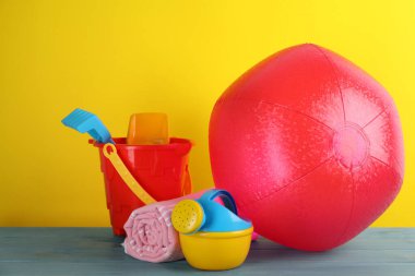 Parlak plaj topu, battaniye ve kumsal oyuncakları açık mavi ahşap masa üzerinde sarı arka planda