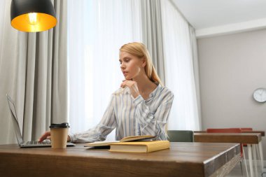 Dizüstü bilgisayarı olan genç bir kadın kütüphanede ders çalışıyor.