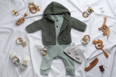 Beyaz çarşaf üzerinde bebek kıyafetleri ve aksesuarları olan düz bir kompozisyon.