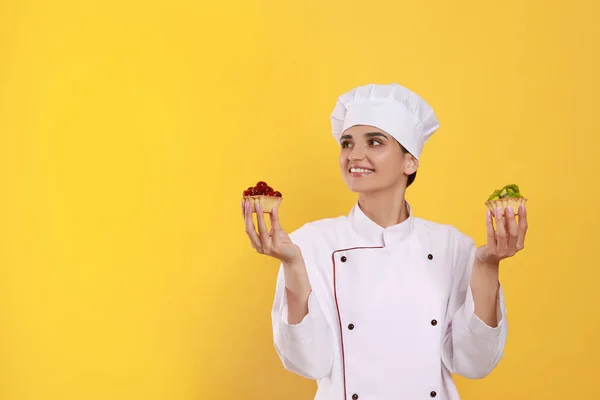 Boldog Professzionális Cukrász Egyenruhában Finom Süteményekkel Sárga Háttérrel Szöveg Helye — Stock Fotó