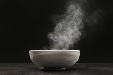 Gri masada koyu arkaplanda buharlı seramik kâse