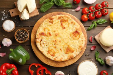 Peynirli lezzetli khachapuri ahşap masada farklı ürünlerle çevrili.