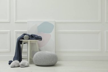 Beyaz duvarın yanında örülmüş puf, tüylü terlikler ve dekor elementleri. Metin için boşluk