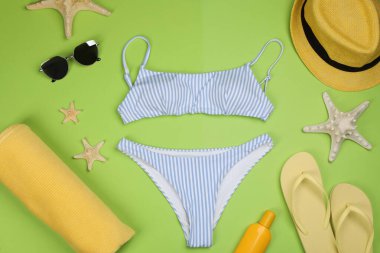 Yeşil arka planda mayolu ve plaj aksesuarlı düz kompozisyon