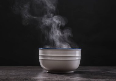 Gri masada koyu arkaplanda buharlı seramik kâse