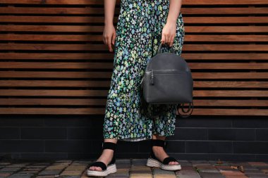 Ahşap duvarın yanında şık sırt çantalı genç bir kadın, yakın plan.