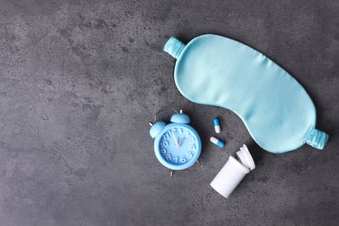 Gri arka planda uyku maskesi, haplar ve alarm saati, mesaj için yeri olan bir daire. Uykusuzluk tedavisi