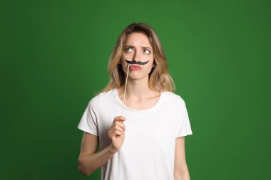 Yeşil arka planda sahte bıyıklı düşünceli bir kadın.