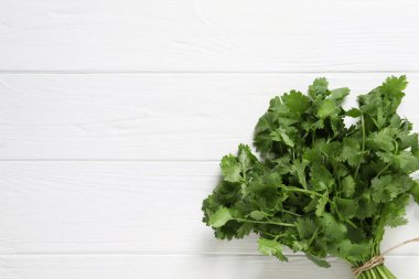 Beyaz ahşap masa üzerinde taze aromatik kişniş demeti, üst manzara. Metin için boşluk