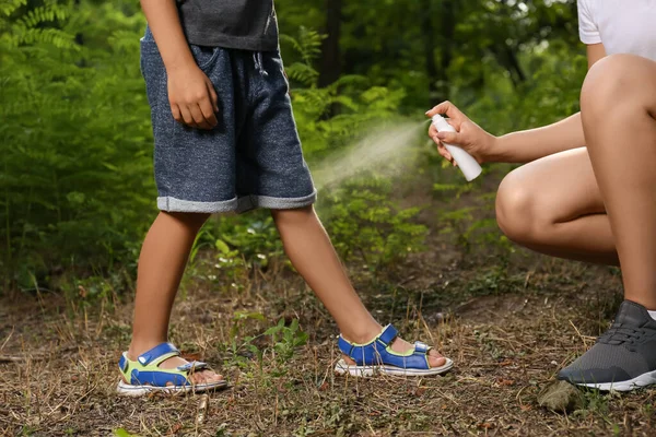 Woman applying insect repellent on her son\'s leg in park, closeup. Tick bites prevention