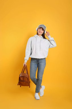 Sarı arka planda şık deri çantalı ve kulaklıklı güzel bir genç kadın.