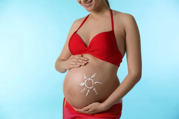 若いです妊娠中の女性とともに太陽の保護クリーム腹の上にライトブルーの背景 — ストック写真